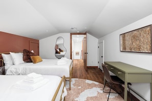 A modern bedroom with two beds, a desk, and a large mirror.