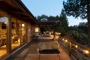 A wooden deck with outdoor furniture, a stone wall, and a glass door leading to an interior space. - Mountain Oasis, Sleeps 24, Hot tub, Game room (Oakhurst)
