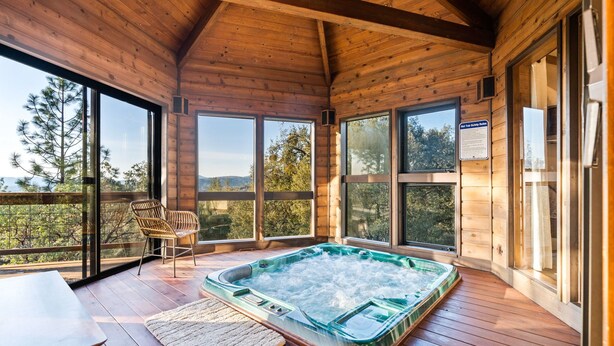 Una cabaña de madera con jacuzzi, ventanas amplias y vistas al bosque.