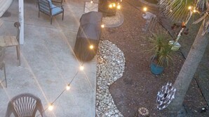 Une terrasse extérieure agrémentée de guirlandes lumineuses, de sièges et d’un petit espace jardin.