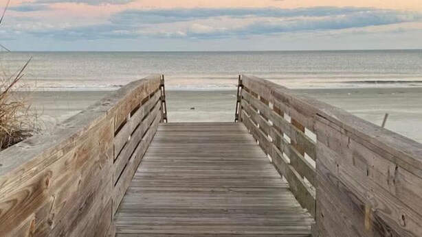 Une promenade en bois mène à une plage sous un ciel nuageux.