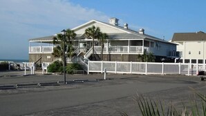 Une maison située en bord de mer, dotée d’un balcon, d’un escalier menant à l’entrée et d’une clôture blanche.