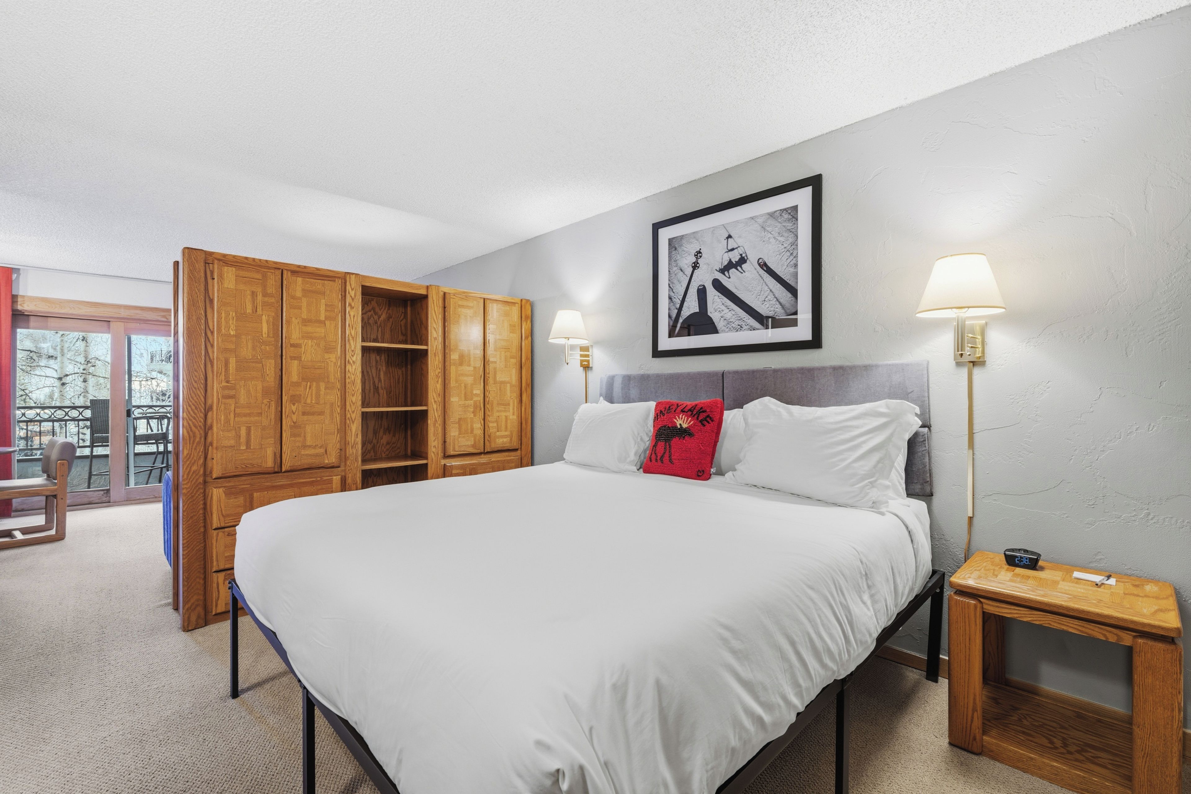 Une chambre à coucher avec un lit, une armoire en bois, deux lampes de chevet, un tableau encadré au mur et une petite table avec une lampe.