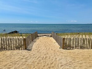 A sandy beach with a wooden fence leading to the water, clear skies, and a calm sea.