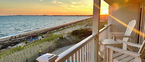 A wooden deck with white railings overlooking a beach with a fence and a pier.