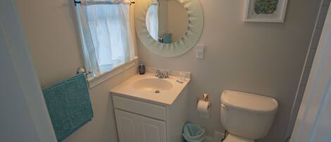 A bathroom with a sink, mirror, toilet, and a window with a curtain.