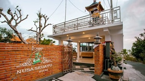The entrance of Nusa Sedayu Hotel with a brick wall, a gate, and a balcony overlooking the interior. - Nusa Sedayu hotel (Penida Island)