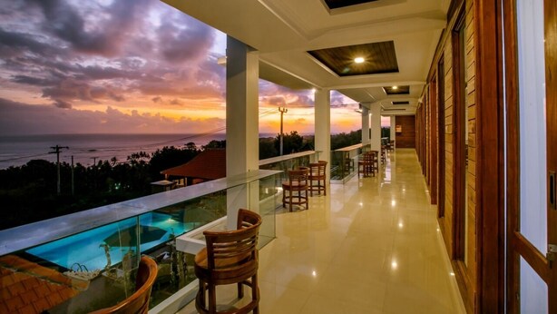 A balcony with a glass railing overlooking a pool and a sunset view. - Nusa Sedayu hotel (Penida Island)