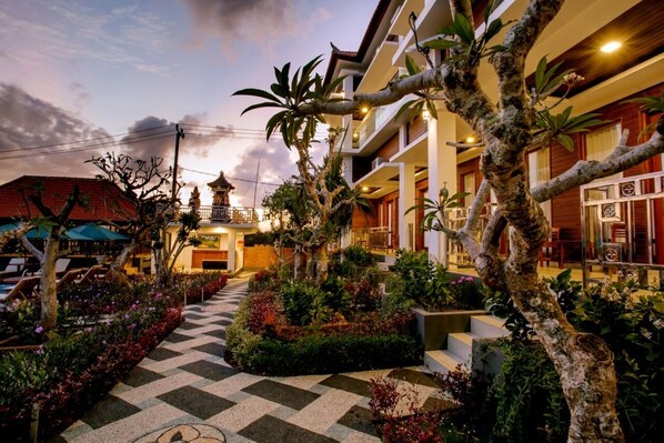 A hotel courtyard with a checkered pathway, potted plants, and a traditional building with a balcony.