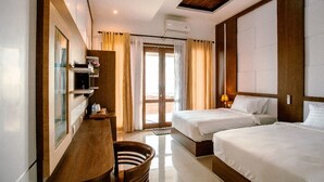 A hotel room with two beds, a desk, a chair, and a large window with curtains. - Nusa Sedayu hotel (Penida Island)