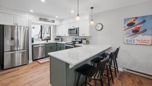 Una cocina moderna con electrodomésticos de acero inoxidable, una isla blanca y taburetes de bar.