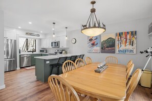 A modern kitchen with white cabinets, stainless steel appliances, and a wooden dining table with chairs. - Beautifully Updated 3bd + Loft / 2ba with Mountain Views / Sleeps 8 (Lincoln)