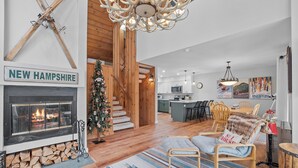 Una sala de estar acogedora con chimenea, una escalera de madera y una cocina al fondo.