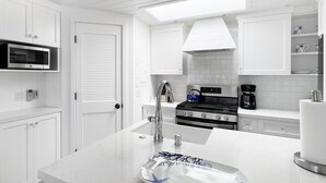 Una cocina moderna con armarios blancos, un microondas de acero inoxidable, una estufa a gas y una cafetera.