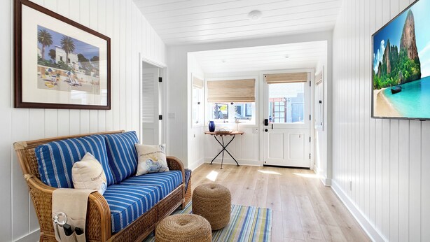 Un salón acogedor con un sofá azul a rayas, un sillón de mimbre y un televisor que muestra una playa tropical.