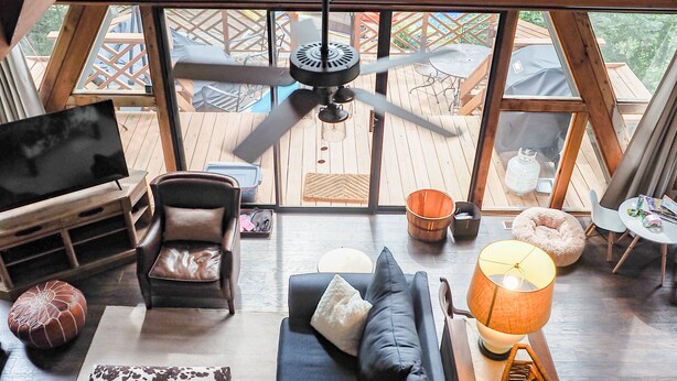 Un loft spacieux avec un grand plafond en bois, un ventilateur de plafond, un canapé en cuir noir, une table basse et une vue sur un lac, visible à travers de grandes fenêtres.