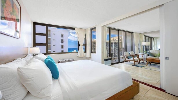 A hotel room with a large bed, a balcony with a view, and a dining area.
