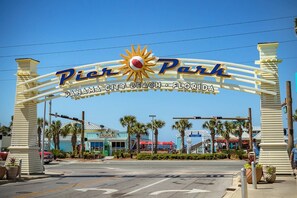 A entrada do Pier Park, com um emblema de sol, palmeiras e um edifício com a inscrição 'Hooko' ao fundo.