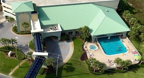 An aerial view of a hotel with a large swimming pool, a covered area, and a parking lot.