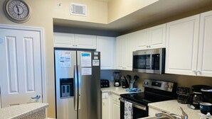A modern kitchen with white cabinets, stainless steel appliances, a refrigerator with a water dispenser, a microwave, a stove, and a sink.