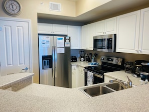 A modern kitchen with white cabinets, stainless steel appliances, a refrigerator with a water dispenser, a microwave, a stove, and a sink. - 🌴 Beach Chairs Included-7th floor 2-King & Bunkroom Directly On the Beach (Panama City Beach)