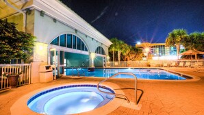 A swimming pool area with a hot tub, palm trees, and a building with arched windows.