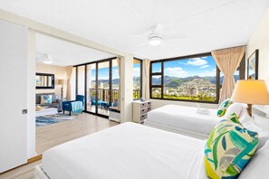 Een hotelkamer met twee bedden, een balkon, een plafondventilator en uitzicht op een stadsgezicht.