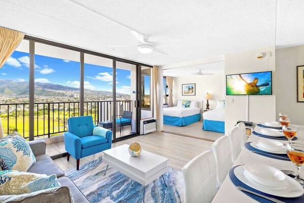 A modern hotel room with a balcony, a dining area, and a TV.