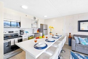 Eine moderne Küche mit weißen Schränken, einem eingebauten Backofen und einem Essbereich mit einem langen Tisch, gedeckt für vier Personen.