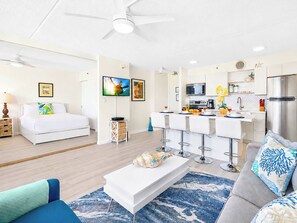 Een moderne hotelkamer met een bed, een televisie, een kitchenette en een zithoek met een salontafel en stoelen.