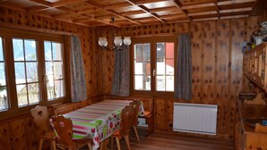 Una habitación revestida de madera con una mesa de comedor, sillas, una araña y ventanas amplias.