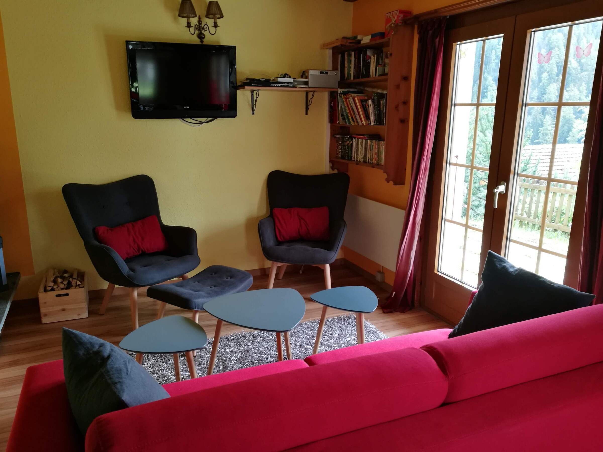 A living room with a red sofa, two armchairs, a coffee table, a TV, and a bookshelf.