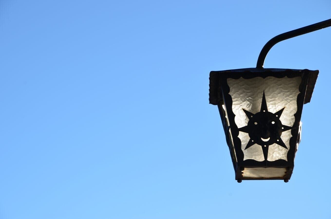 Eine Straßenlampe mit einem sternförmigen Glaskopf vor blauem Himmel.