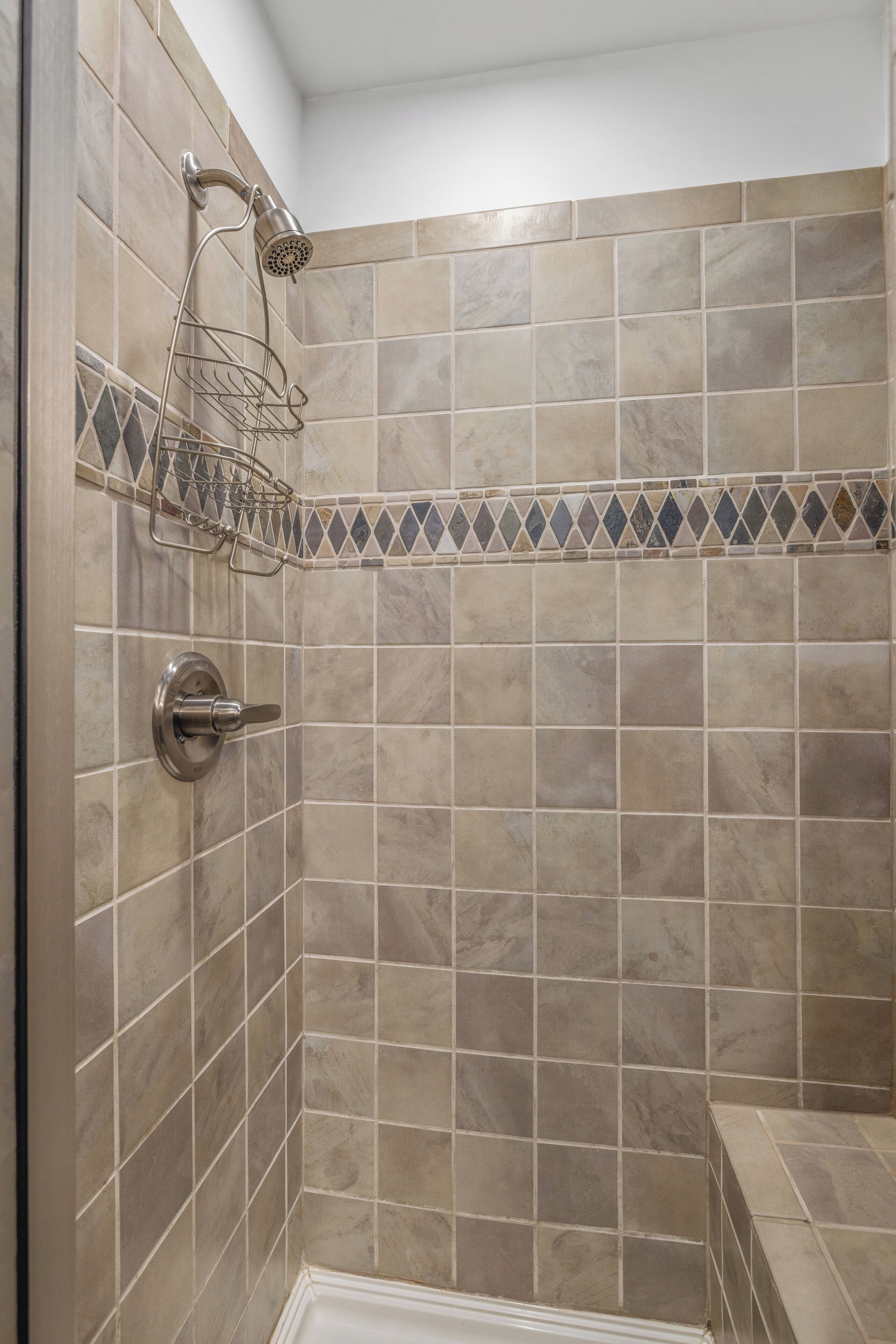 Un área de ducha con baldosas color beige, un cabezal de ducha y un perchero de metal.