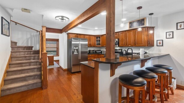 Una cocina moderna con armarios de madera, un refrigerador de acero inoxidable y una zona de bar con taburetes.