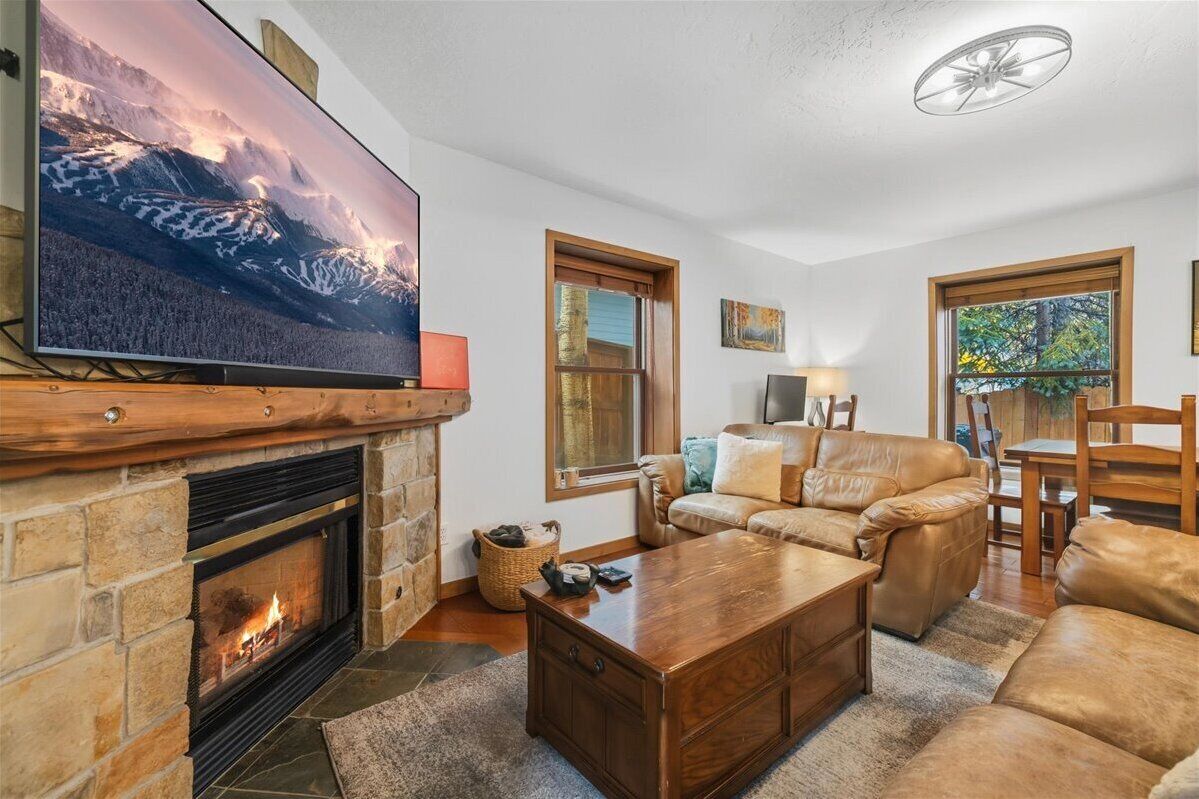 Una sala de estar acogedora con chimenea, sofá de cuero y un televisor de pantalla plana colgado en la pared.