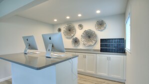 A modern kitchen with two Apple iMacs on a counter, white cabinets, and decorative wall art. - Americas Best Value Inn Ocean Shores (Ocean Shores)