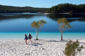 A beach with two people walking, trees, and a calm lake. - Woolshed Eco Lodge (Scarness)