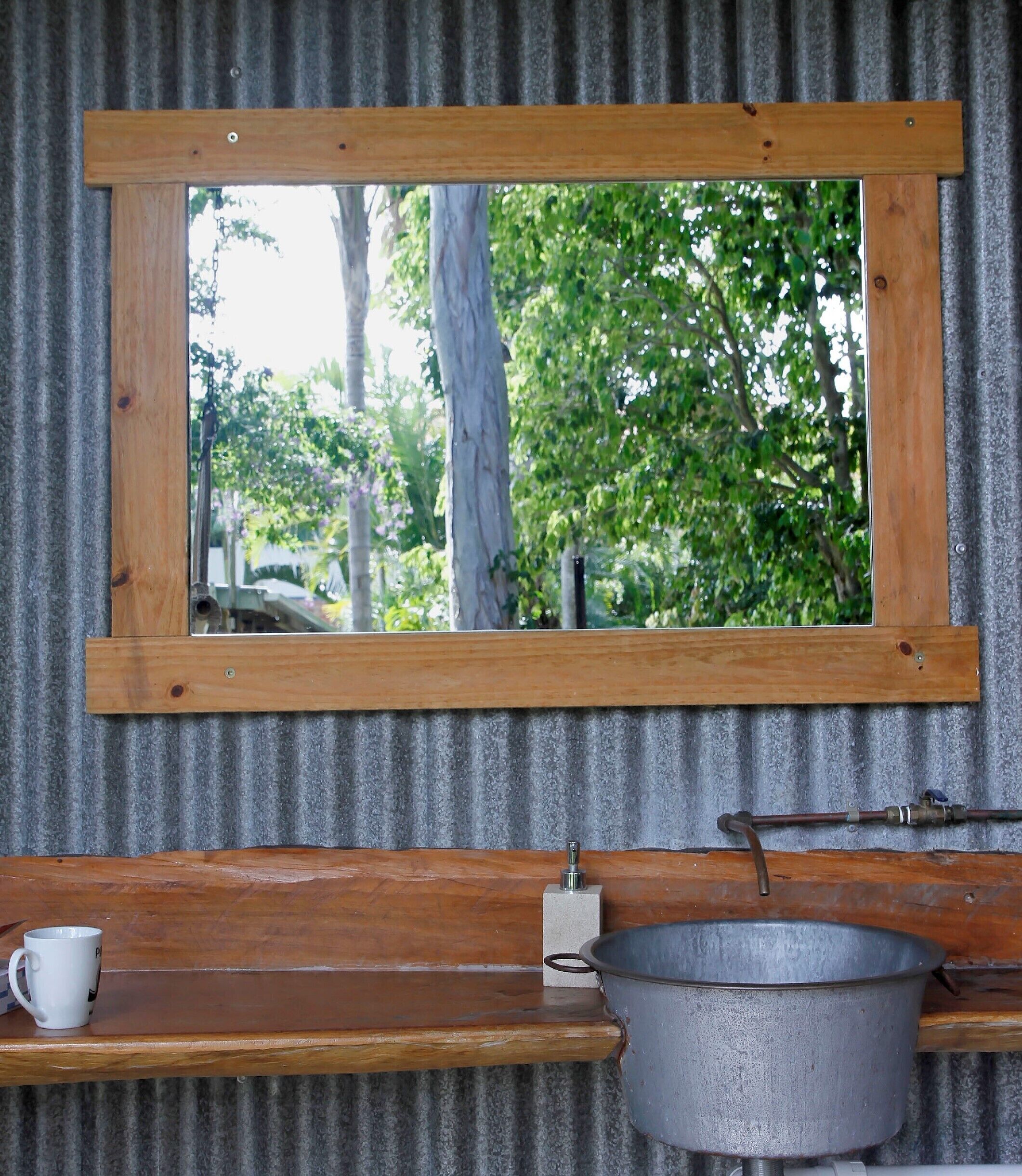Ein rustikales Badezimmer mit einem spiegelnden Holzerahmen, einem Metallwaschbecken und einer Holzablage mit einer Tasse.