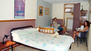A hotel room with a large bed, a bedside table, a chair, and a small kitchenette area.