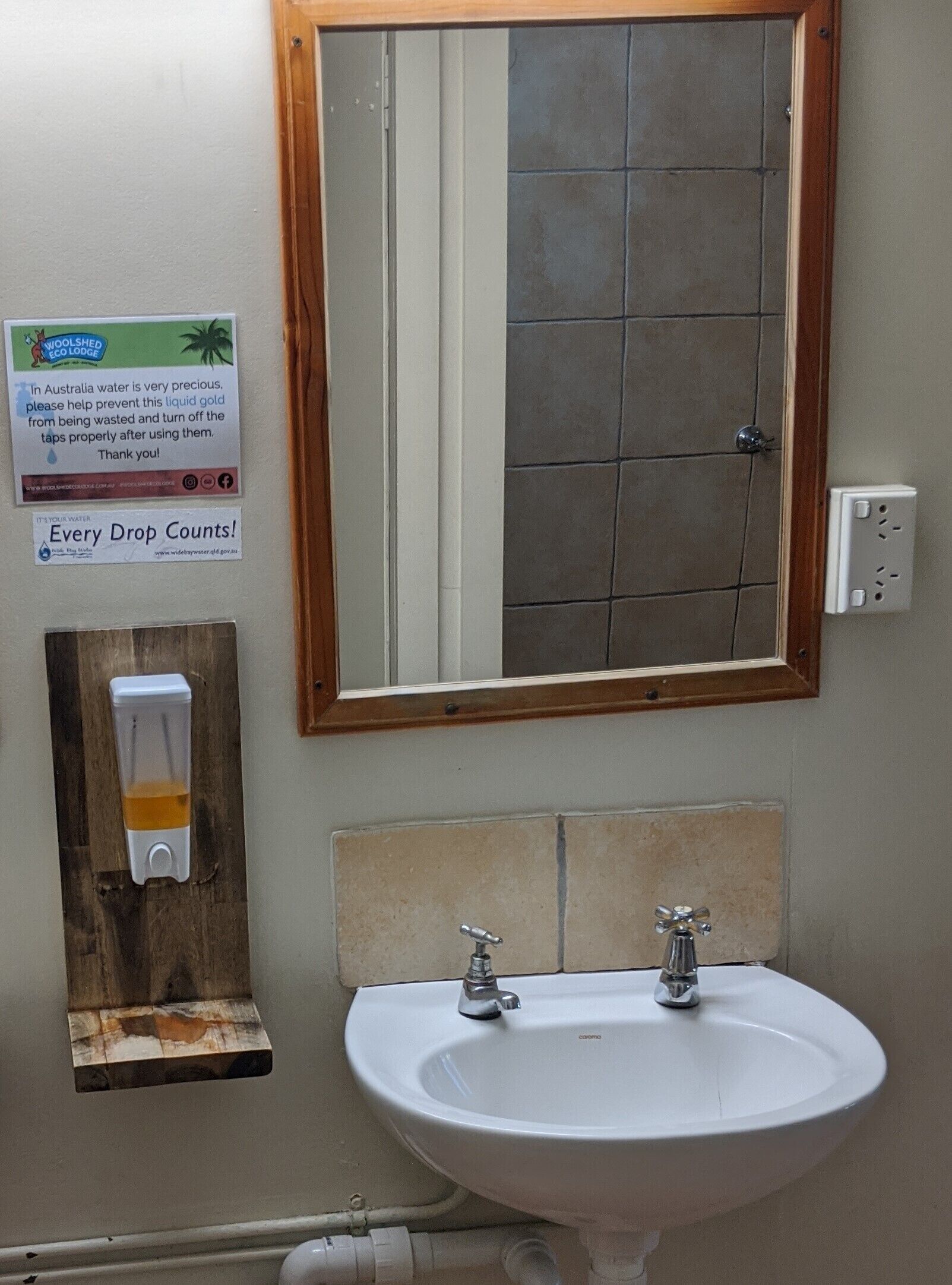Un baño con lavamanos, espejo y dispensador de jabón fijado en un panel de madera.