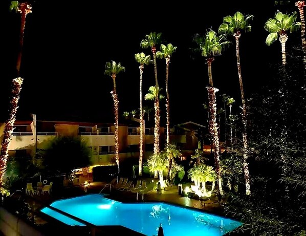 Relax by the illuminated pool surrounded by palm trees and lounge chairs.