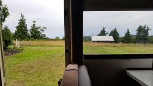 A view from inside a vehicle, looking out through a window at a grassy field with trees and a white building in the distance. - RV/Motor Home by LAVENDER FARM! Free HIGH SPEED BEST INTERNET=WORK from HOME W/D (Sequim)