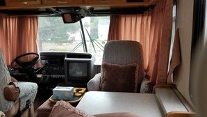 A cozy RV interior with a wooden dashboard, a comfortable seating area, and a small table with a box and a pillow. - RV/Motor Home by LAVENDER FARM! Free HIGH SPEED BEST INTERNET=WORK from HOME W/D (Sequim)