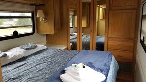 A compact RV bedroom with a bed, a window, and wooden cabinets. - RV/Motor Home by LAVENDER FARM! Free HIGH SPEED BEST INTERNET=WORK from HOME W/D (Sequim)