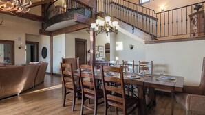 A spacious dining area with a wooden table set for six, surrounded by wooden chairs. A chandelier hangs above the table, and a staircase with a wrought iron railing leads to an upper level. - Stunning W/Mountain Views + Hot Tub + Close to Skiing - Overlook Chalet (Steamboat Springs)
