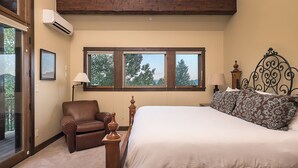 A bedroom with a large bed, a chair, a nightstand, and a window with a view of trees. - Stunning W/Mountain Views + Hot Tub + Close to Skiing - Overlook Chalet (Steamboat Springs)