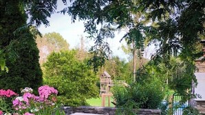 A garden with a stone bench, flowering plants, and a wooden structure in the background.