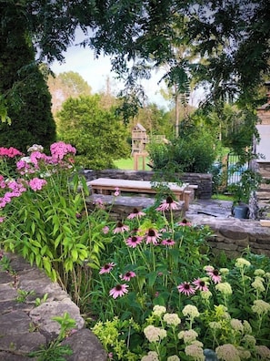 A garden with a stone bench, flowering plants, and a wooden structure in the background.