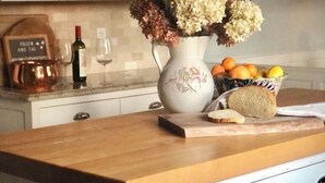 A kitchen with a wooden countertop, a vase with flowers, a bowl of fruit, and a wine bottle.
